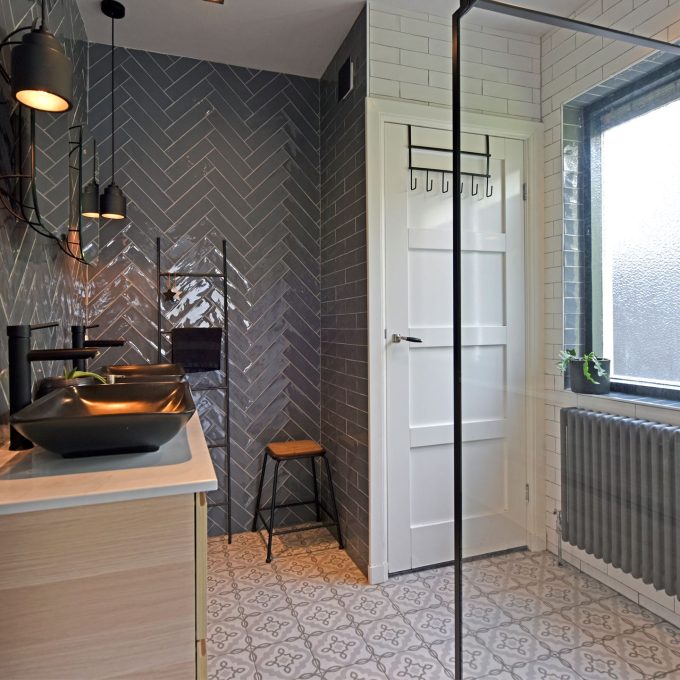 Badkamer met keramische patroontegel, grijze visgraat tegels op de wand, en paneeldeur